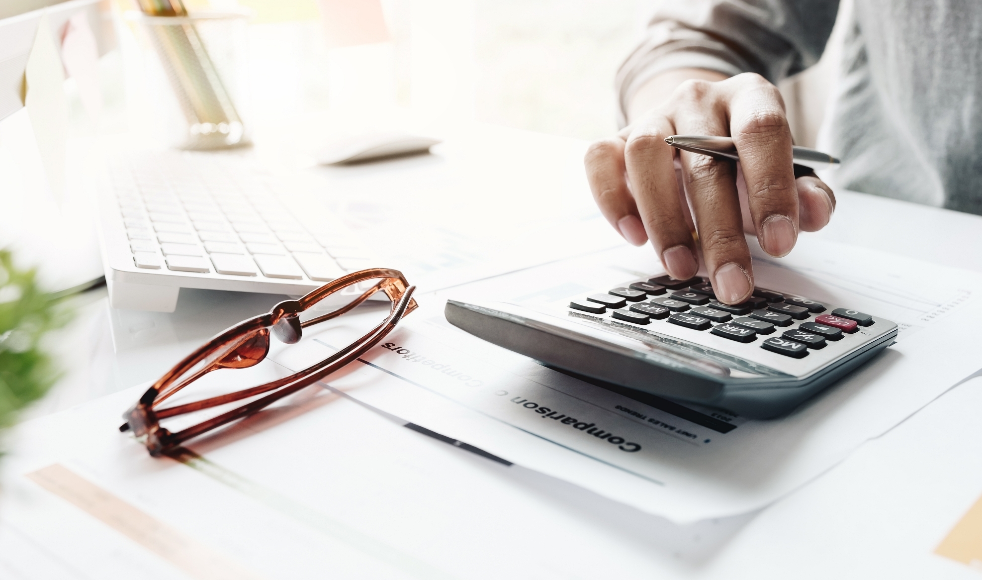 Close up of businessman or accountant hand holding pencil working on calculator to calculate financial data report, accountancy document and laptop computer at office, business concept