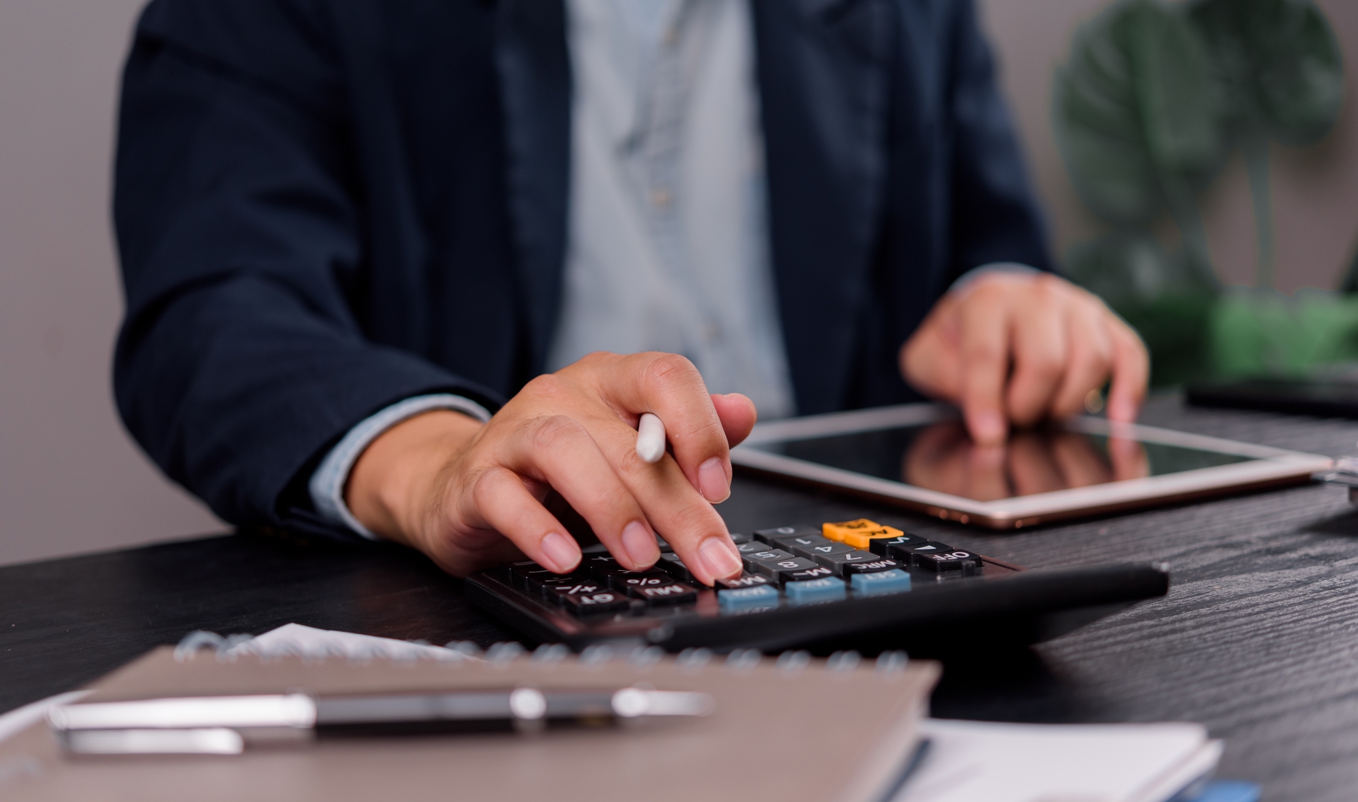 Close-up of a businessman calculating finances with a calculator and tablet, focusing on financial management and budgeting tasks at a desk.